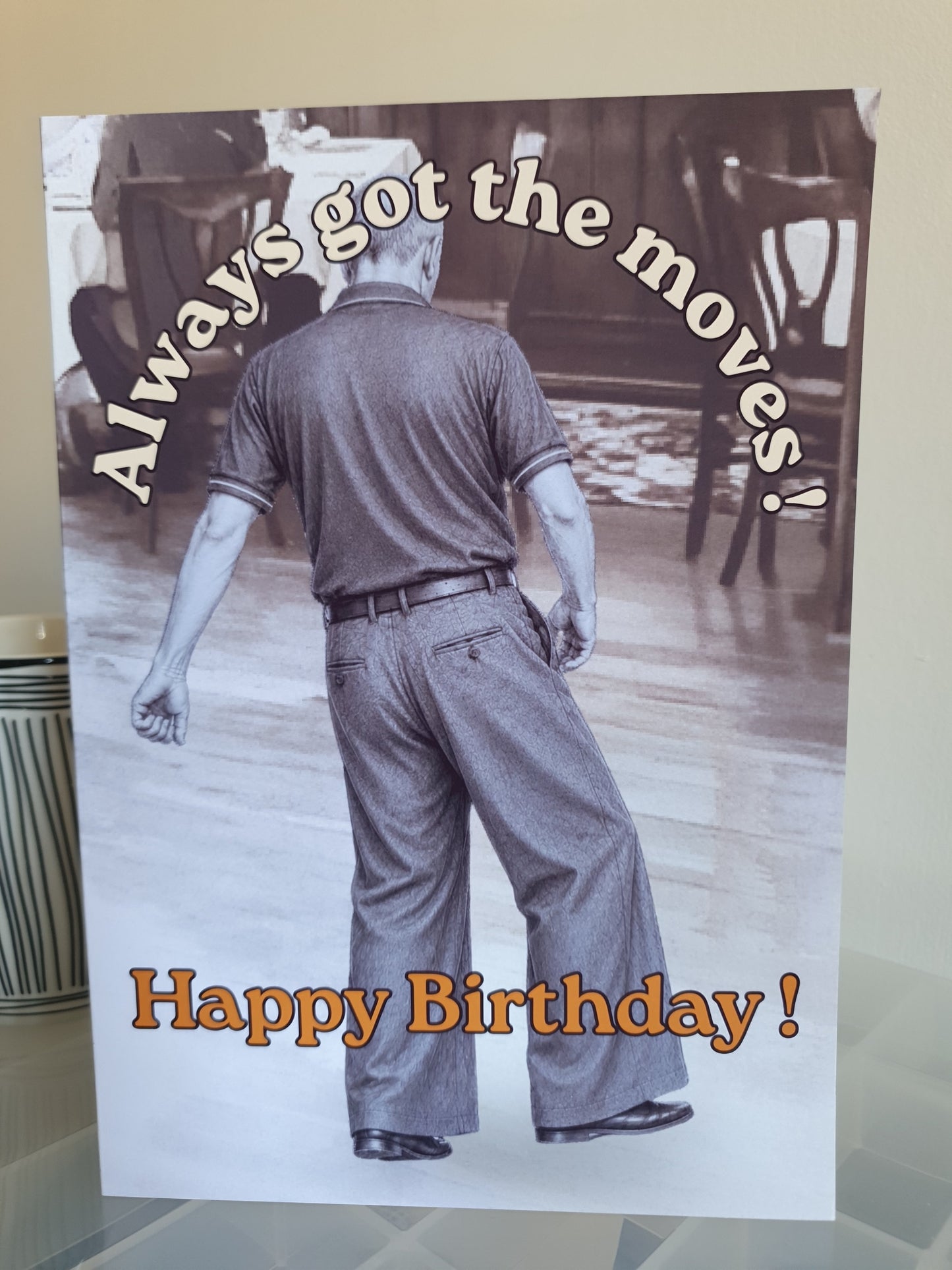 A northern soul card on a small plastic top next to a mug depicting the monochrome image of northern soul man middle aged in polo shirt and wide leg trousers dancing with text stating always got the moves