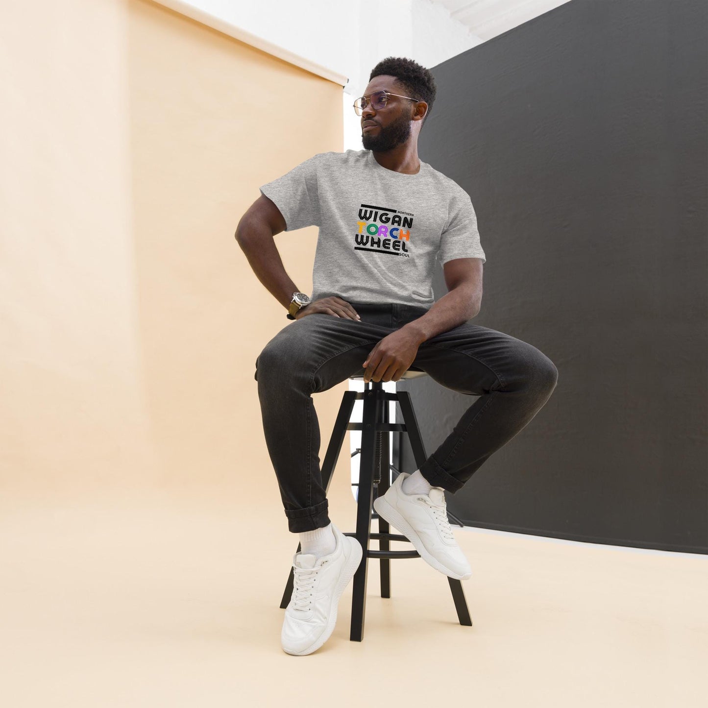 Man sitting on a stool wearing a gray t-shirt with colorful textstating the NORTHERN soul word Wigan Torck Wheel