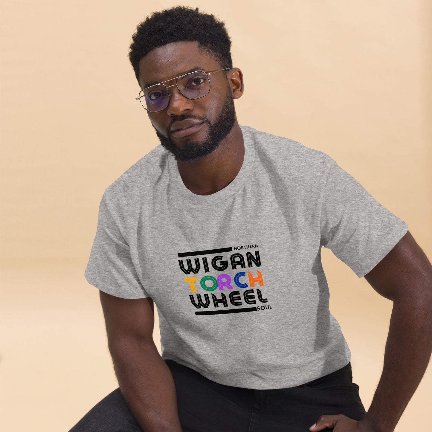 Man wearing a gray t-shirt with 'Wigan Torch Wheel' text on a beige background