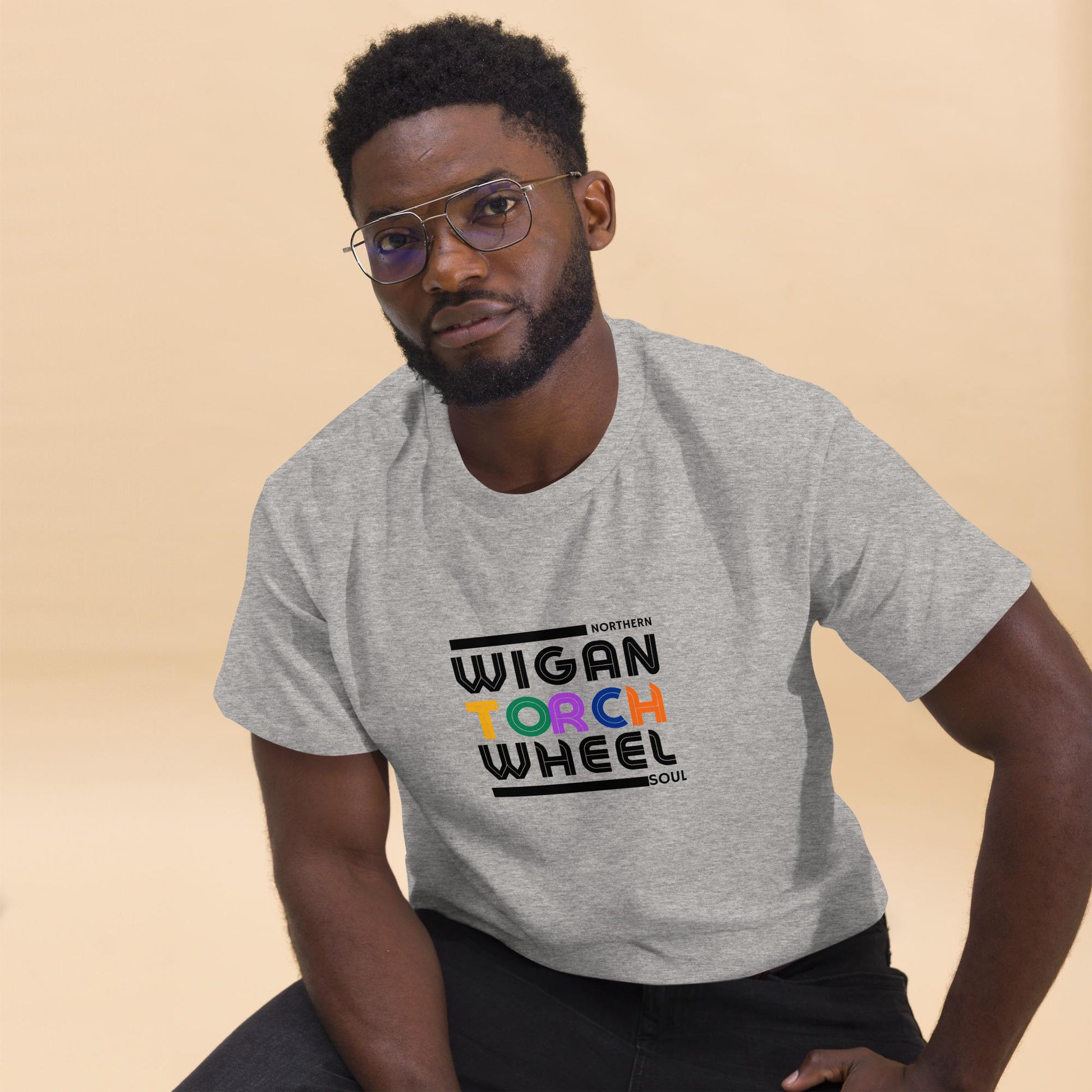 Man wearing a gray t-shirt with 'Wigan Torch Wheel' text on a beige background