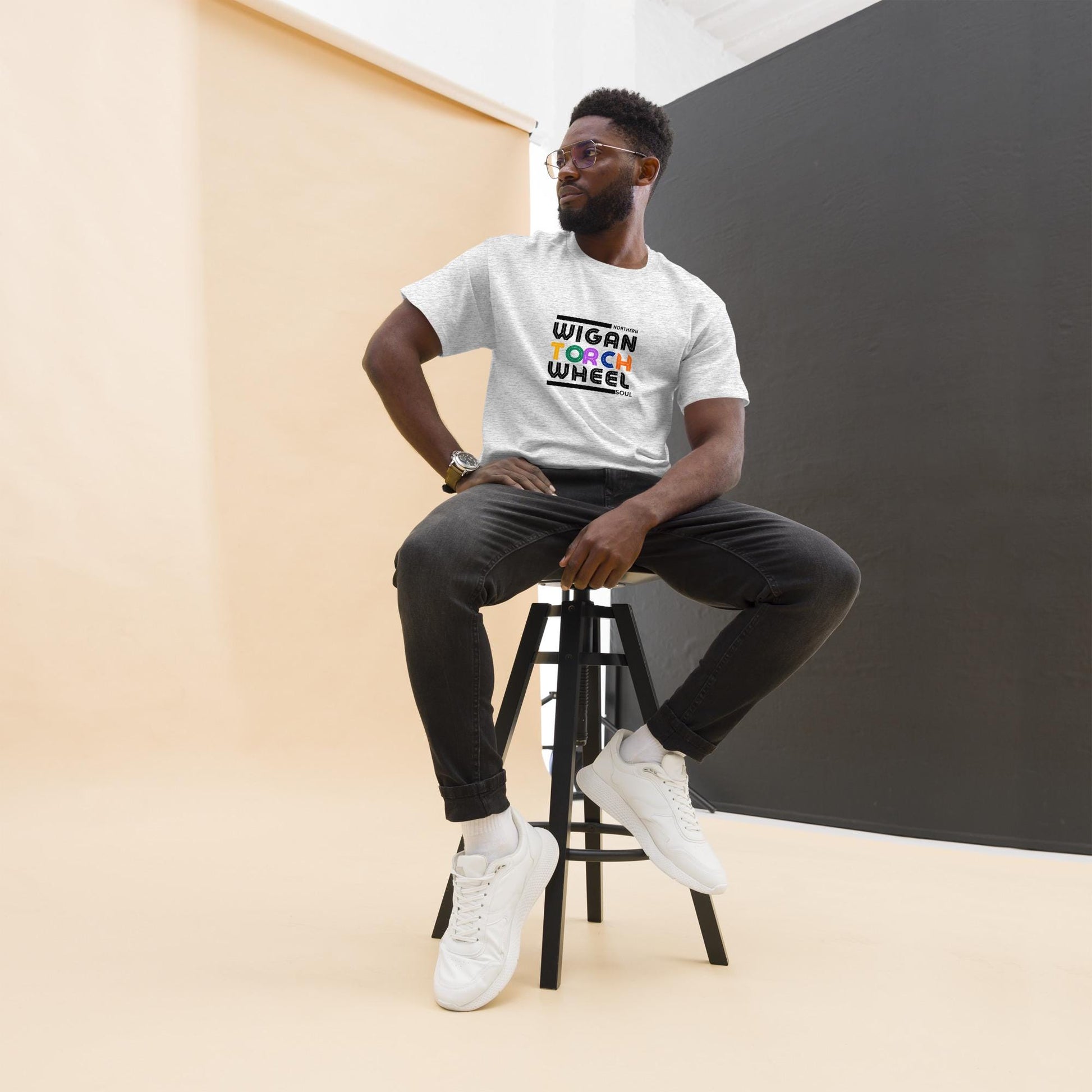 Man sitting on a stool wearing a white t-shirt with colorful text design of wigan torch wheel