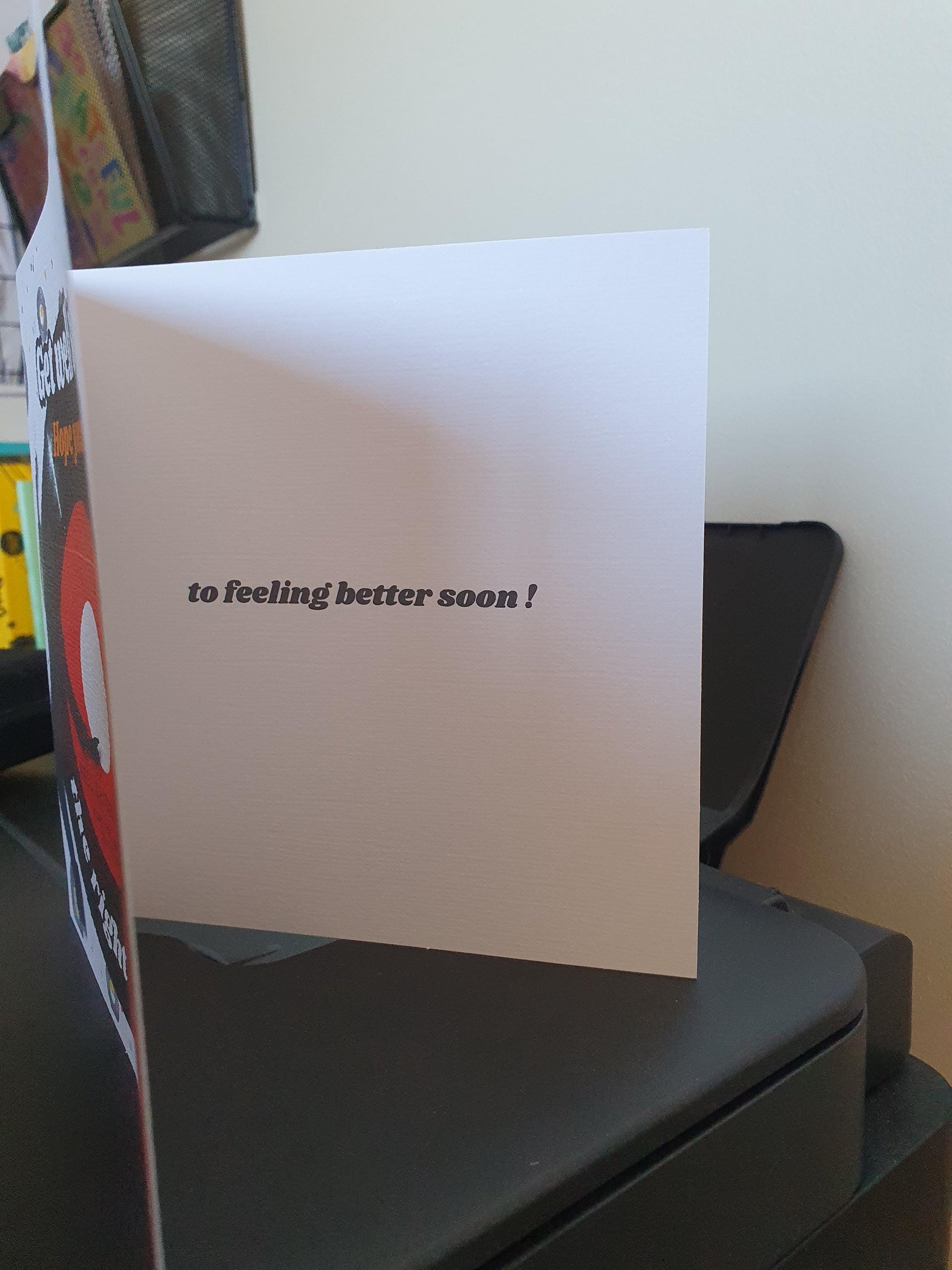 White card with 'to feeling better soon!' text on a desk.