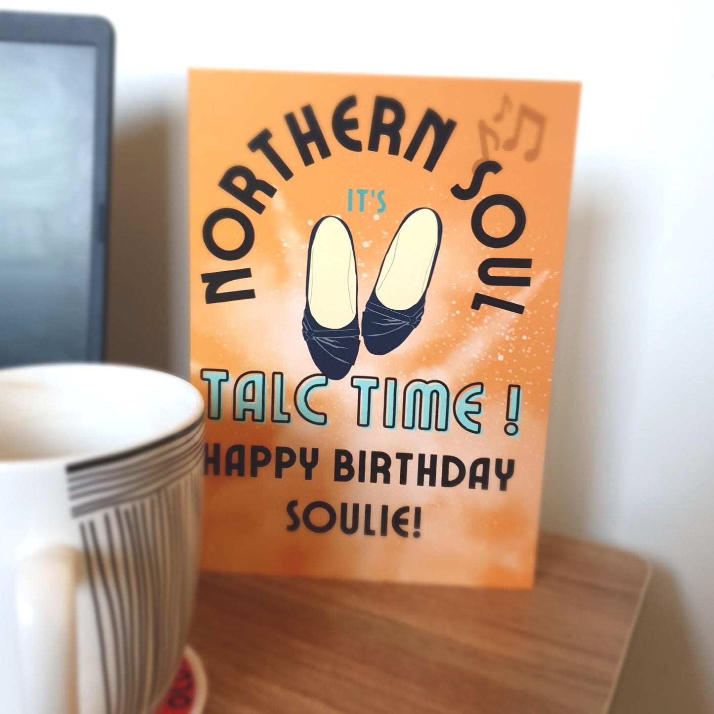 Greeting card with 'Northern Soul' text and birthday message to a soulie on an orange background, next to a cup.