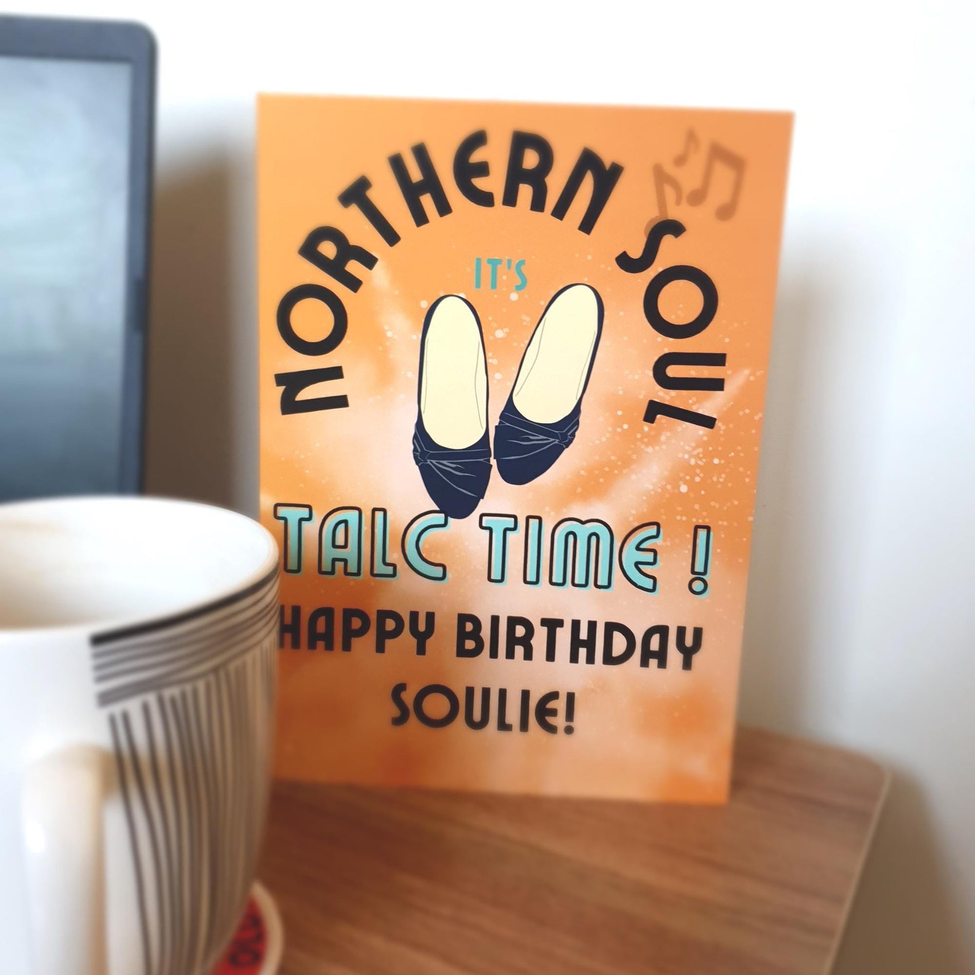 Greeting card with 'Northern Soul' text and birthday message to a soulie on an orange background, next to a cup.