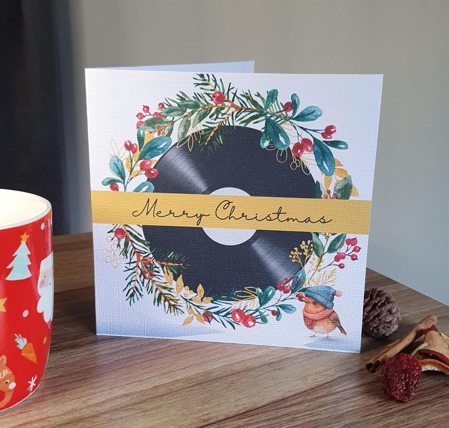 Christmas card with vinyl record design on a wooden surface with a mug and decorative items.