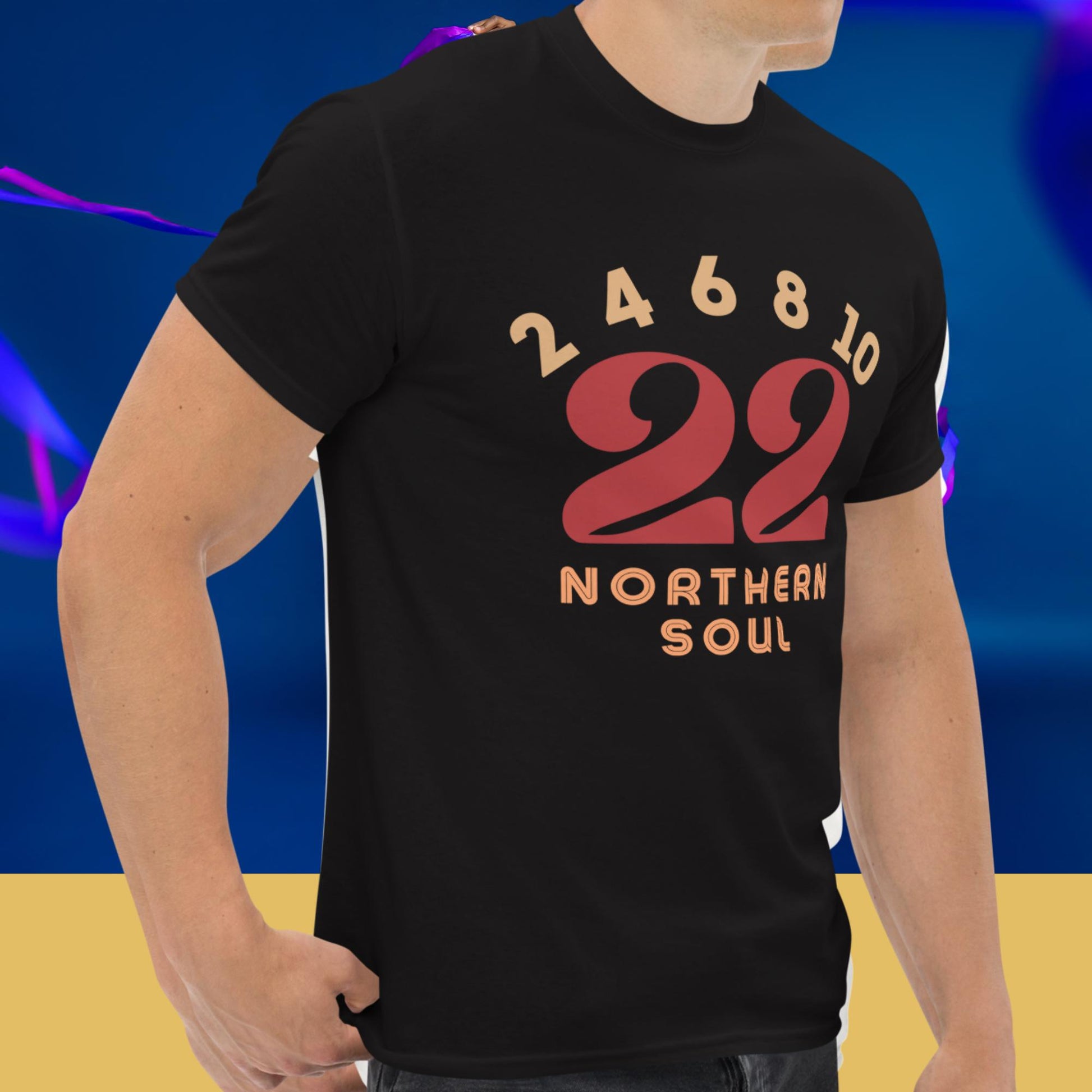Person wearing a black t-shirt with red and orange text and numbers 2 4 6 8  10 on a blue and yellow gradient background